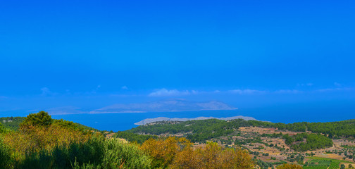 Panoramic view of the coastal rocks of the Mediterranean Sea, overgrown with green forest in the early summer morning. Rhodes island, Greece.