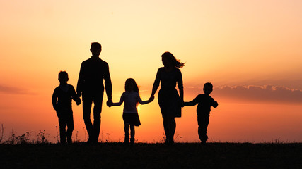 Silhouettes of happy family holding the hands in the meadow during sunset.