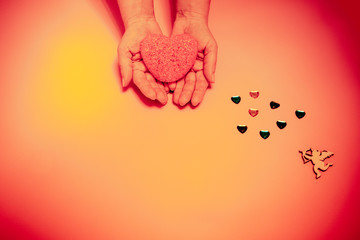 on a pink, beige background a red heart in human hands and an angel nearby.