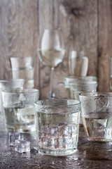 Many glasses of water splashed with drops and pieces of ice on a gray table