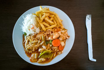 Thai Sweet and spicy chicken with fries, salad and vegetables on white plate, with fork on the right
