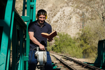 Young construction worker reading a book on old railway bridge