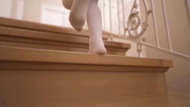 Close-up of the legs of a little girl in white tights walking up the wooden stairs at home
