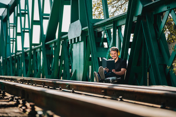 Young construction worker reading a book on old railway bridge