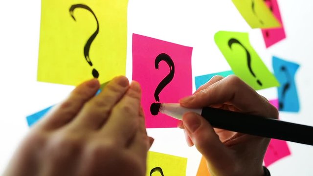 Businesswoman writing question marks on colorful sticky note paper on office whiteboard