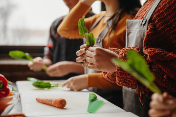 Midsection of students holding leaf vegetables in cooking class