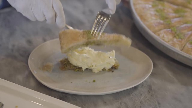 Hands of chef in white rubber gloves preparing eastern sweet kunafa putting melted cheese inside close up. Turkish cuisine concept