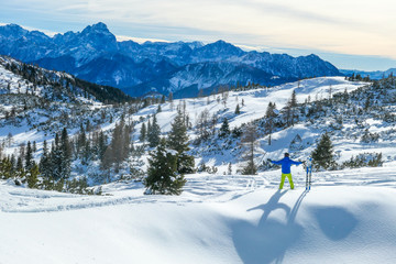 Cloudy morning in Alps, Nassfeld, Austria. Young skier stands on the powder snow with his skies. Mountain slopes covered with snow. Sharp edges of the Alps. Pine trees covered with snow on the slopes.