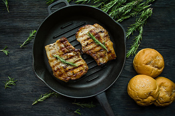 Grilled steak on a round grill pan, decorated with spices for meat, rosemary on a dark wooden background. View from above.