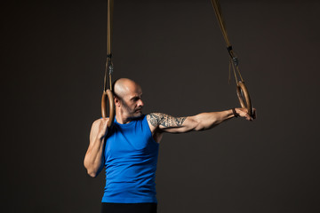 Fototapeta na wymiar Athletic middle aged man training with rings, studio background
