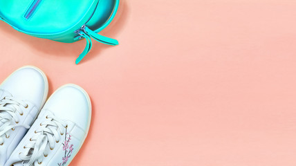Top view White sneakers and turquoise backpak over coral background. Flat lay. Copy space.