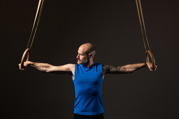 Athletic middle aged man training with rings, studio background