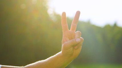 LENS FLARE, DOF: Bright sunbeams shine on male hand and showing the peace sign.