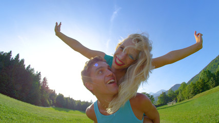 LENS FLARE: Happy man looks into the camera while giving girl a piggyback ride.