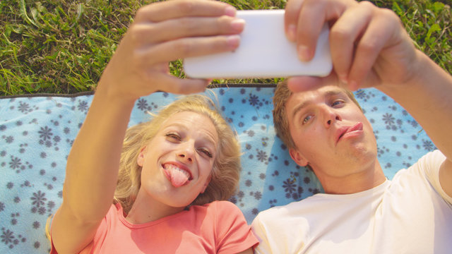 CLOSE UP: Goofy couple making funny faces while taking selfies for social media.
