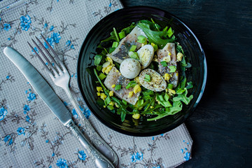 Marinated herring with arugula, onions, boiled quail eggs and lemon juice and olive oil. Delicious salad. Proper nutrition. Dark wooden background.