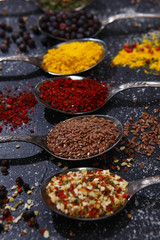 Six table vintage spoons, filled with various seasonings and spices on a dark background. Seasonings and spices are scattered on a dark background. View from above