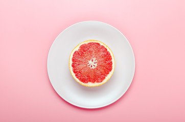 Half a grapefruit on a pink plate on a pink background. Refreshing summer tropical fruit. Minimal...
