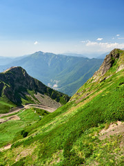 The peaks of a high mountain slope with cable car, in front of which is a valley with residential houses.