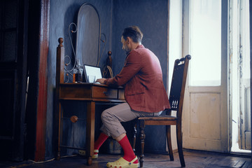 Stylish Man of Brutal Appearance at Home at a Desk Working on a Laptop.