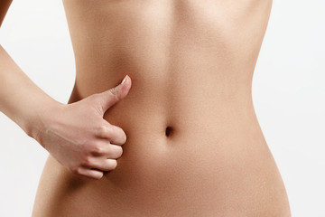 slim, athletic waist of a young woman on white background. The hand in the foreground shows a finger up gesture. the concept of female beauty and health, nutrition and diet, beautiful figure