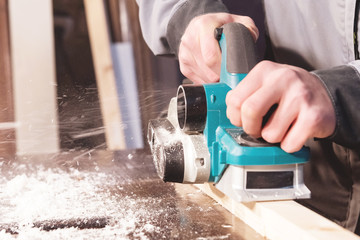 The hands of a carpenter working woodworking power tools. Close up of the work of the electric planer