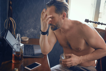 Freelance guy with a naked torso smokes and works on a laptop