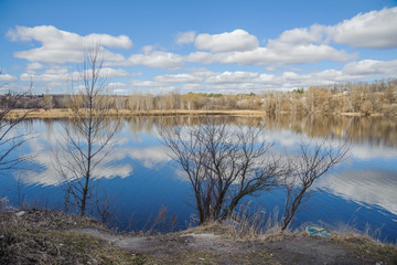 Trees with spring sky and clouds in the reflection of water.