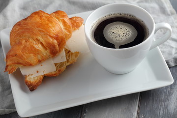 French breakfast: croissant sandwich with cheese and a cup of black coffee