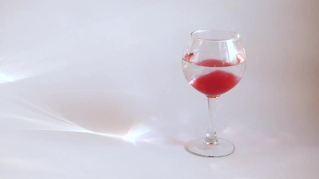 Red paint flow into wineglass with clear water. Imitation of blood or red wine. On white background, with empty space at the left.