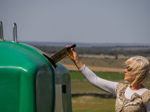 A mature woman pulling a crystal bottle in a green bin for recycling glass
