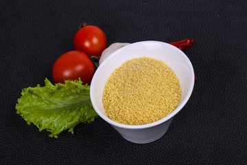 Raw couscous in the bowl served salad leaves, tomato and pepper