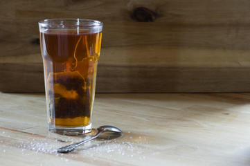 glass of herbal tea on wooden table with sugar sprinkled next to it	
