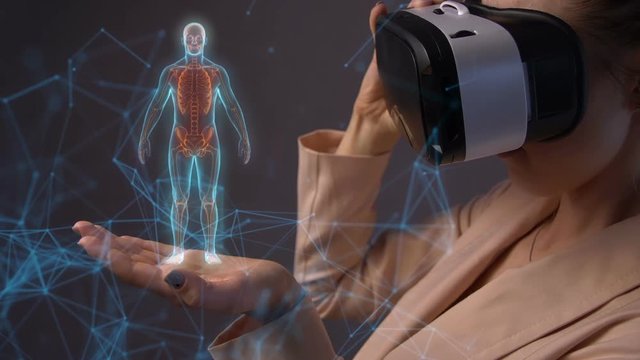 Young woman using a virtual reality headset with hologram rotating humans body skeleton and conceptual network lines and dots in her hand