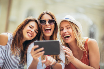 Three happy smiling female friends sharing a tablet computer as they stand close together looking...