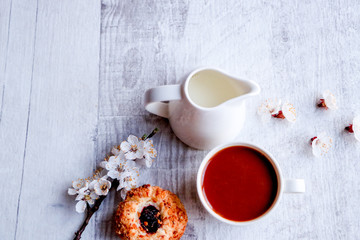 Obraz na płótnie Canvas Closeup of a cup of coffee and a jug of milk next to apricot flowers and homemade cookies on a neutral background.