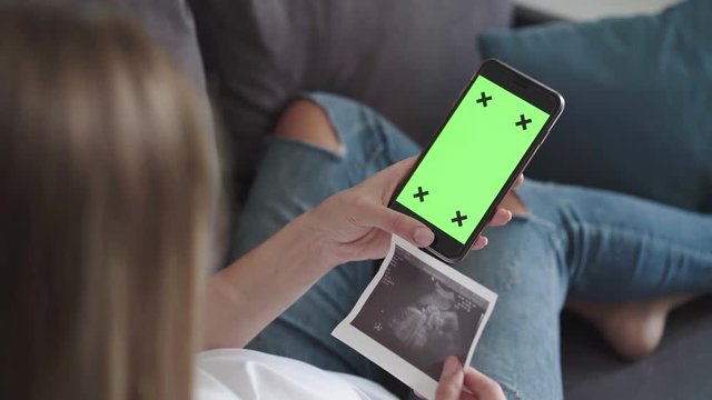 Pregnant woman holds ultra diagnostic snapshot and phone