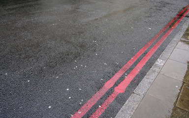Double red line near curb on wet asphalt road. In London these indicate stopping forbidden any time, and are used instead of yellow lines sometimes.