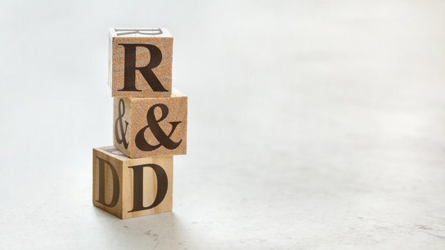 Pile with three wooden cubes - letters R&D meaning Research and Development on them, space for more text / images at right side.