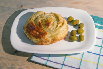 Balkan cuisine. Burek - popular national dish, it is hot cake made with puff pastry. Round burek on a white plate, rustic background