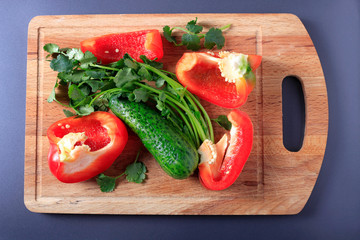 Red pepper, cucumber and greens on a wooden kitchen board, top view