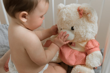 Baby girl playing with a teddy bear in a crib.