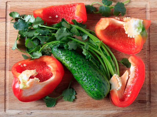 Red bell pepper, cucumber and greens on a wooden background
