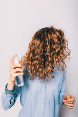 Young woman with long curly hair applying cosmetic care product