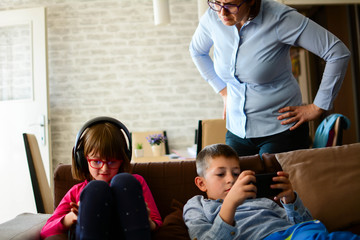 Childhood, technology and family concept - The woman is furious because children sit and play games, listening to music with headphones, smartphones in the living room after school. Horizontal.