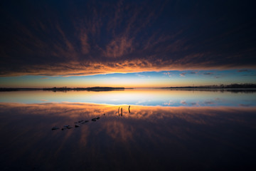 Atmospheric sunset above mirroring water surface with threatening clouds and an impressive landscape