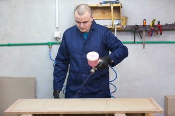 Young man in a furniture factory applies a glue on a wooden piece of the sofa