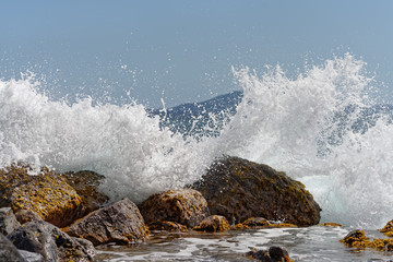 Obraz premium A wave breaks on big stones in the water, thousands of drops of water sparkle in the sunlight, island silhouette in the background, snapshot - Location: Caribbean, island Guadeloupe