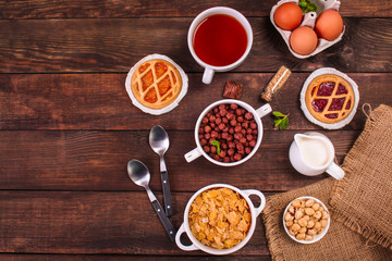 cornflakes, coffee, cottage cheese, bread, butter, eggs, jam and other ingredients for breakfast on a dark background. Top view with copy space