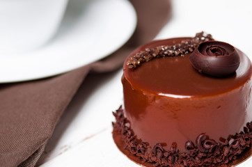 A delicious chocolate cake with chocolate pieces lies on a wooden stand next to a white cup, which stands on a white table